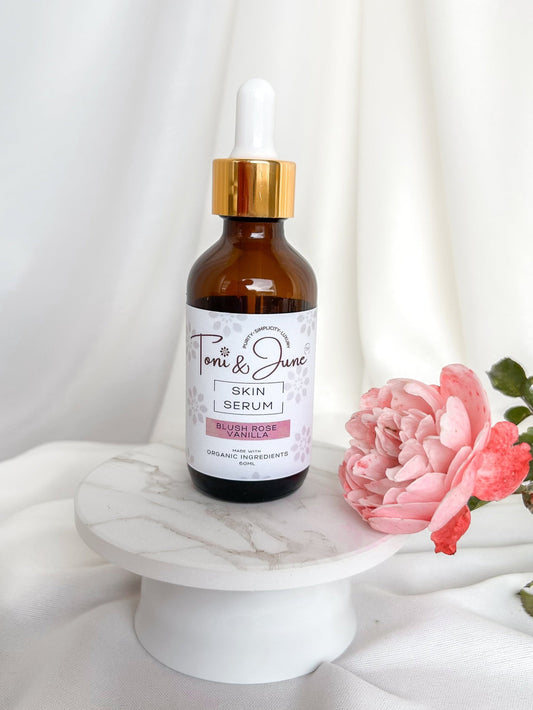 Toni & June blush rose vanilla skin serum bottle on a marble surface with a pink flower.